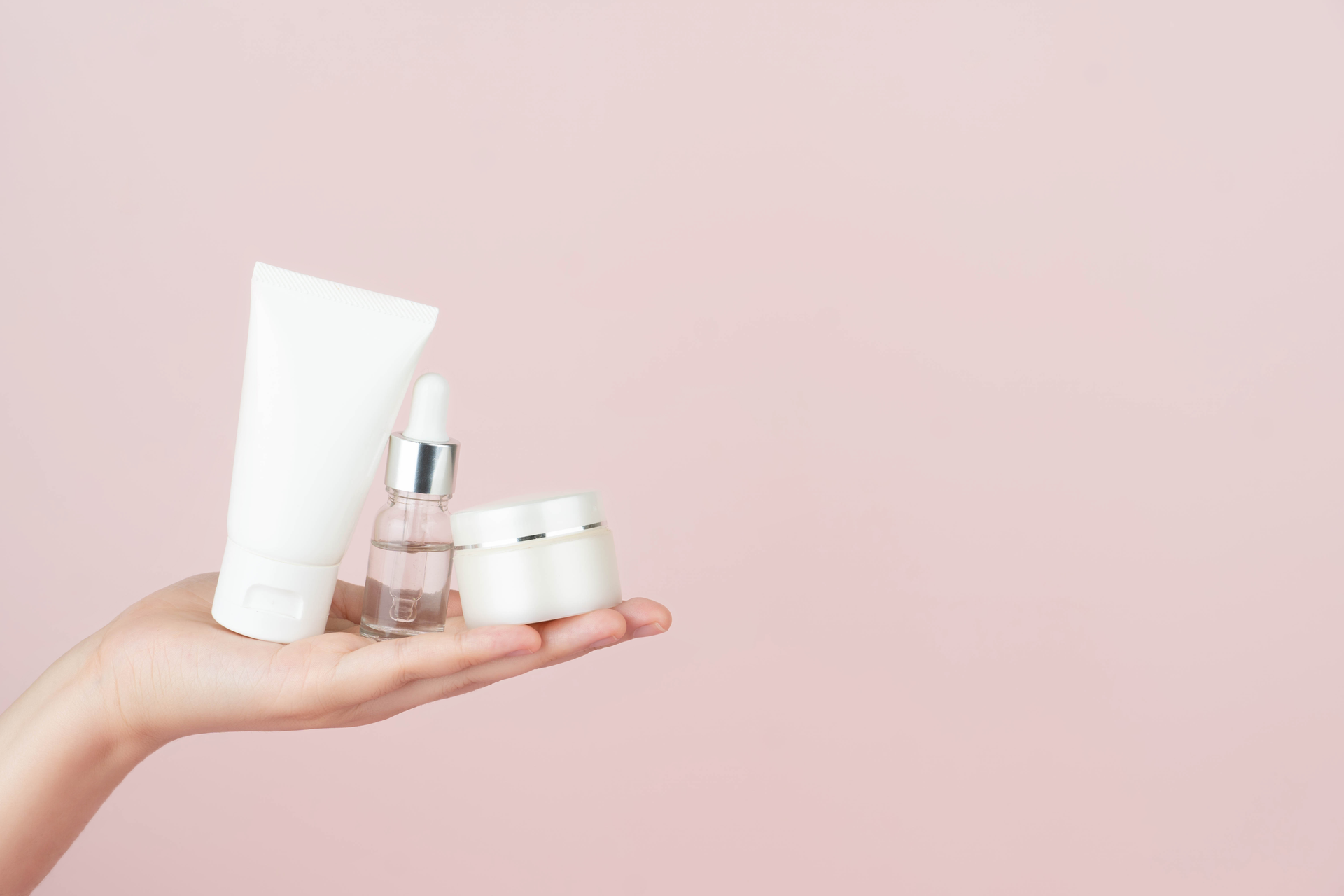 A woman is holding a bottle of lotion and a bottle of serum in her hand.
