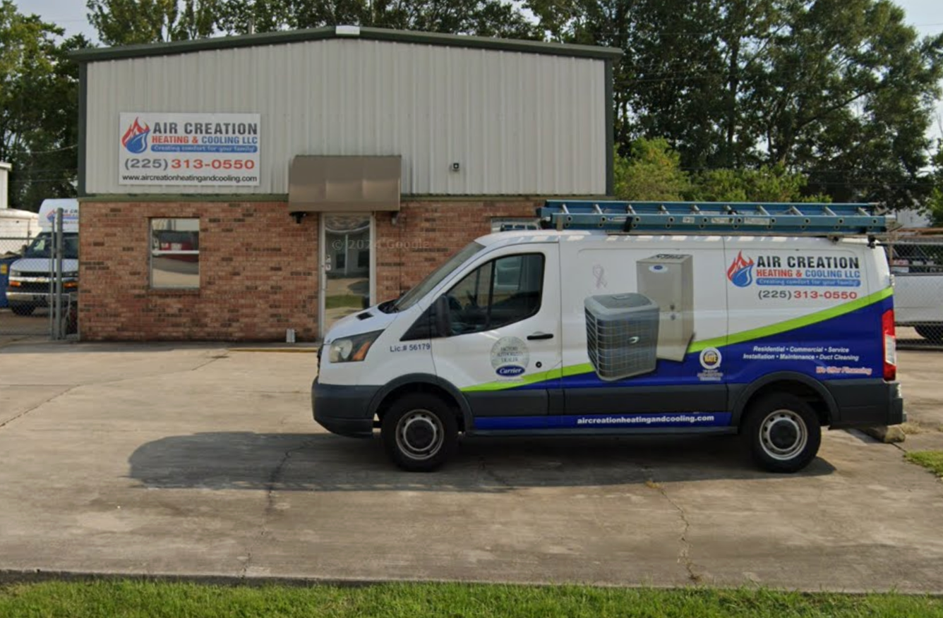 White service van parked outside a brick-and-metal building with company signage and ladders on the roof rack