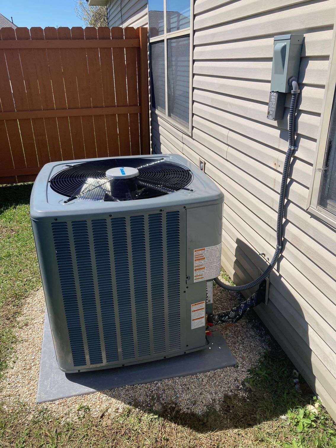 Outdoor Dakin air conditioner unit beside a brick house, with landscaping and a tree nearby