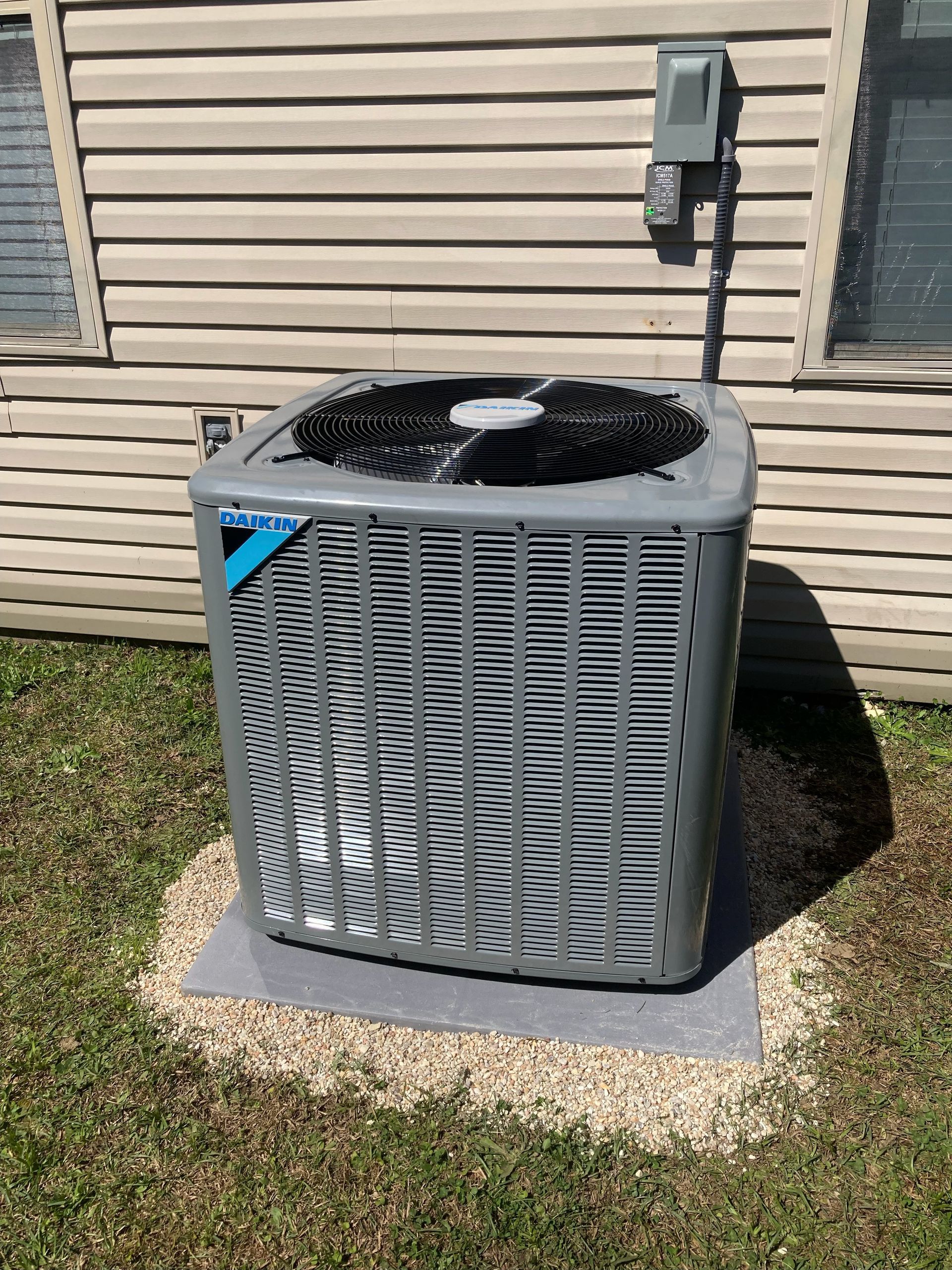 Gray outdoor air conditioner unit beside a beige house wall on a concrete pad.