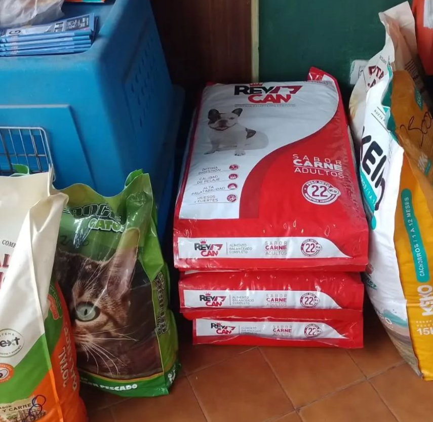 Bolsas de comida para mascotas apiladas en el suelo, incluyendo comida para perros y gatos. Envases rojos, verdes y blancos.