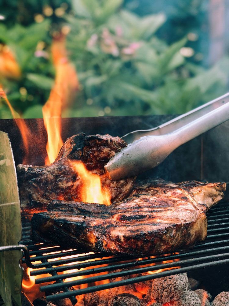 A Steak Is Being Cooked on A Grill with Tongs — Scotto's Food Logistics in Mitchell, ACT