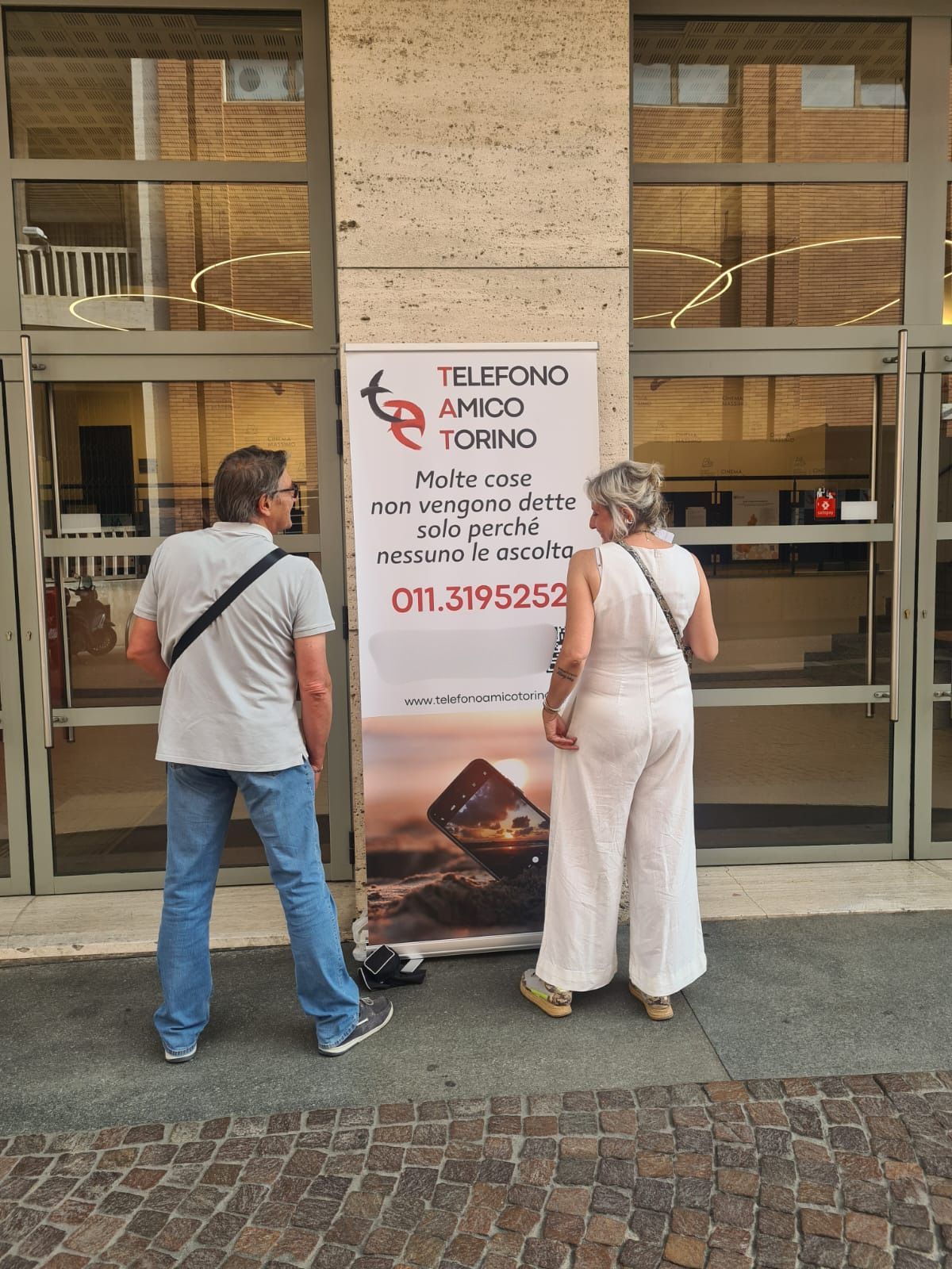 Persone girate di spalle accanto totem Telefono Amico per evento cinema