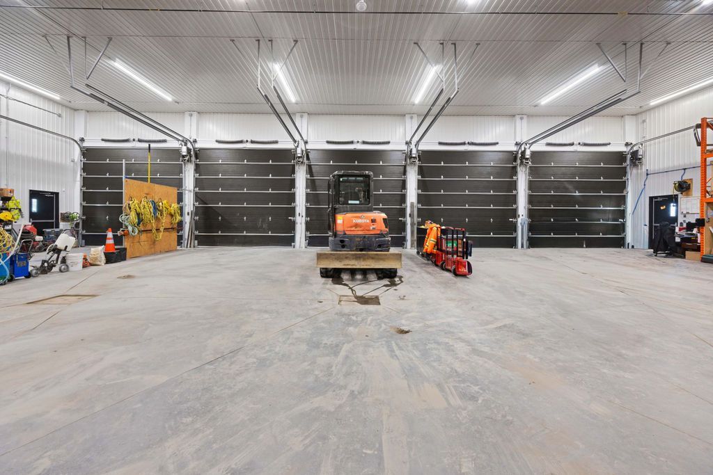 Large empty industrial garage with bright overhead lights, tools, equipment, and vehicles along the walls