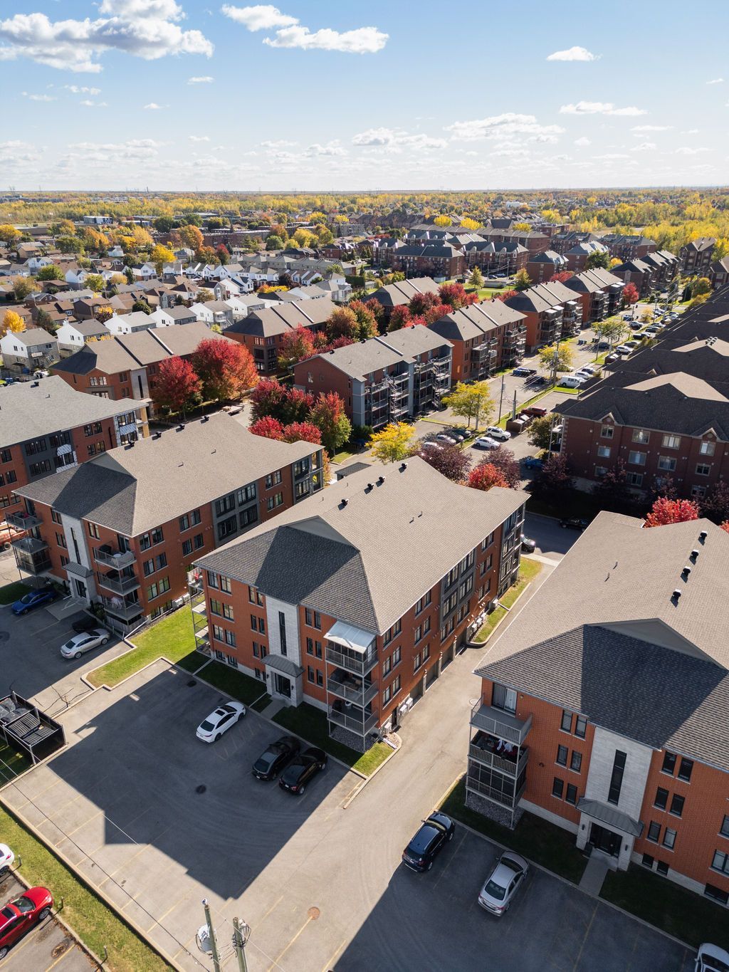 Aerial view of a suburban apartment complex with parking lots and colorful autumn trees under a blue sky