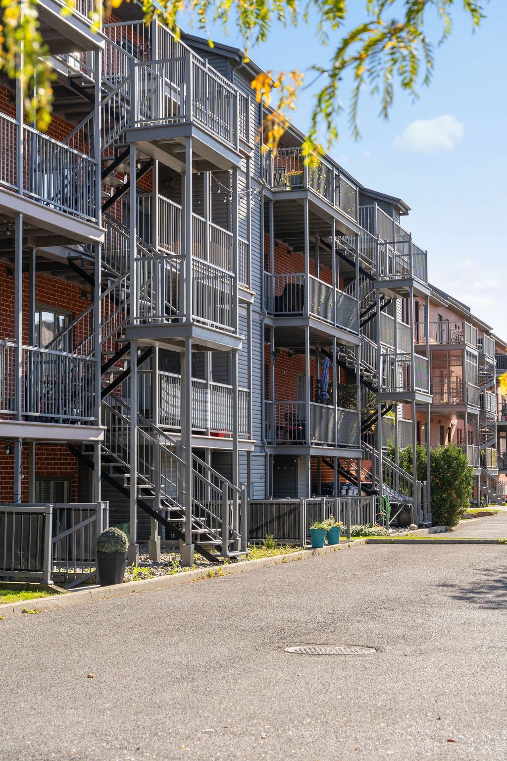 Immeuble d'appartements avec balcons métalliques et escaliers extérieurs le long d'un chemin de gravier sous un ciel bleu