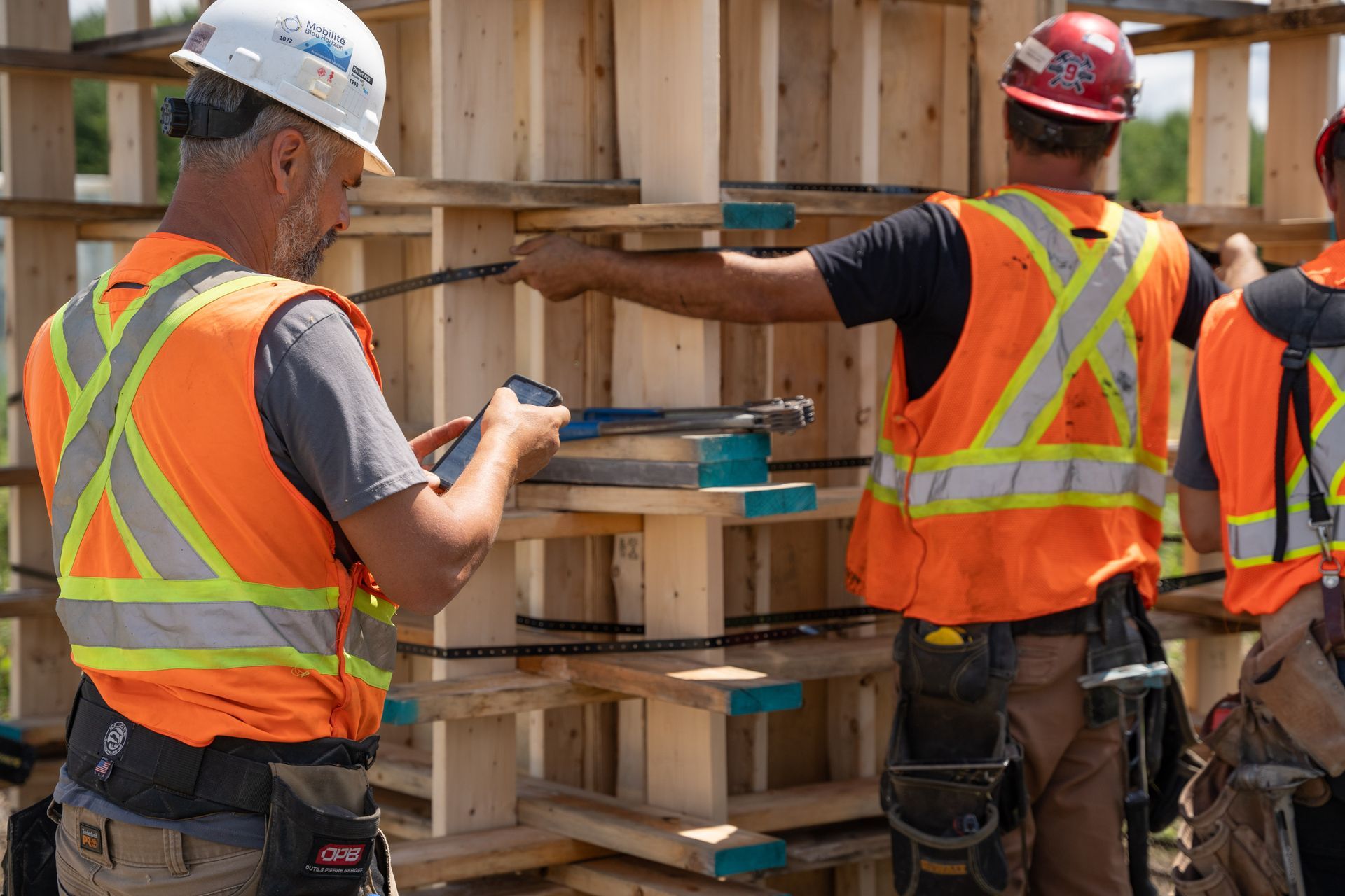 Two construction workers in safety vests and hard hats assembling wood framing on a building site