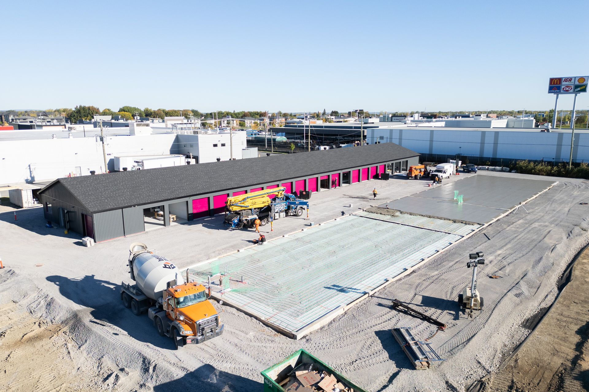 Aerial view of a construction site with a long black building, pink panels, and concrete work area