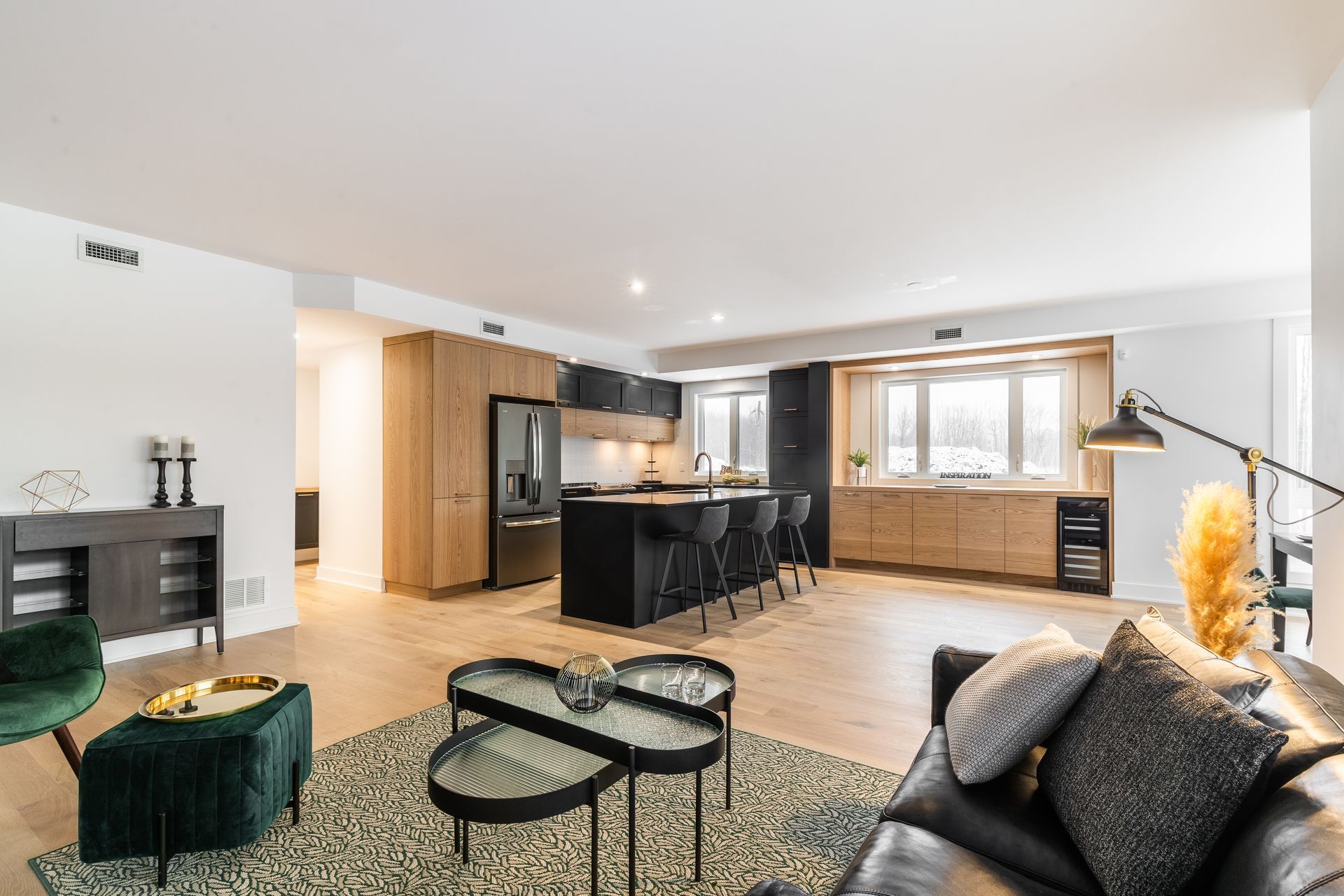 Modern open-plan living room with black sofas, patterned rug, and a kitchen island in back