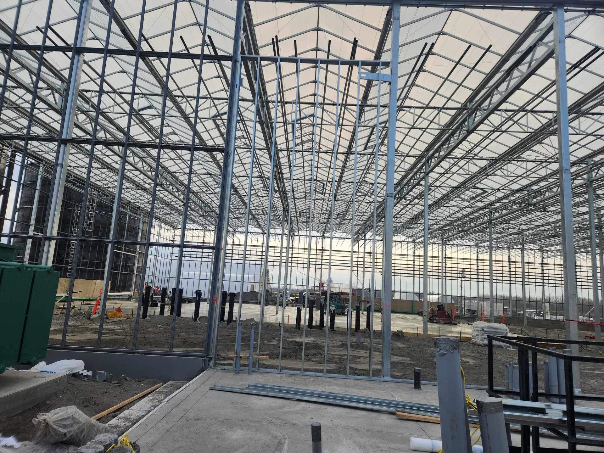 Interior of a steel-framed building under construction with a high white roof and scattered equipment
