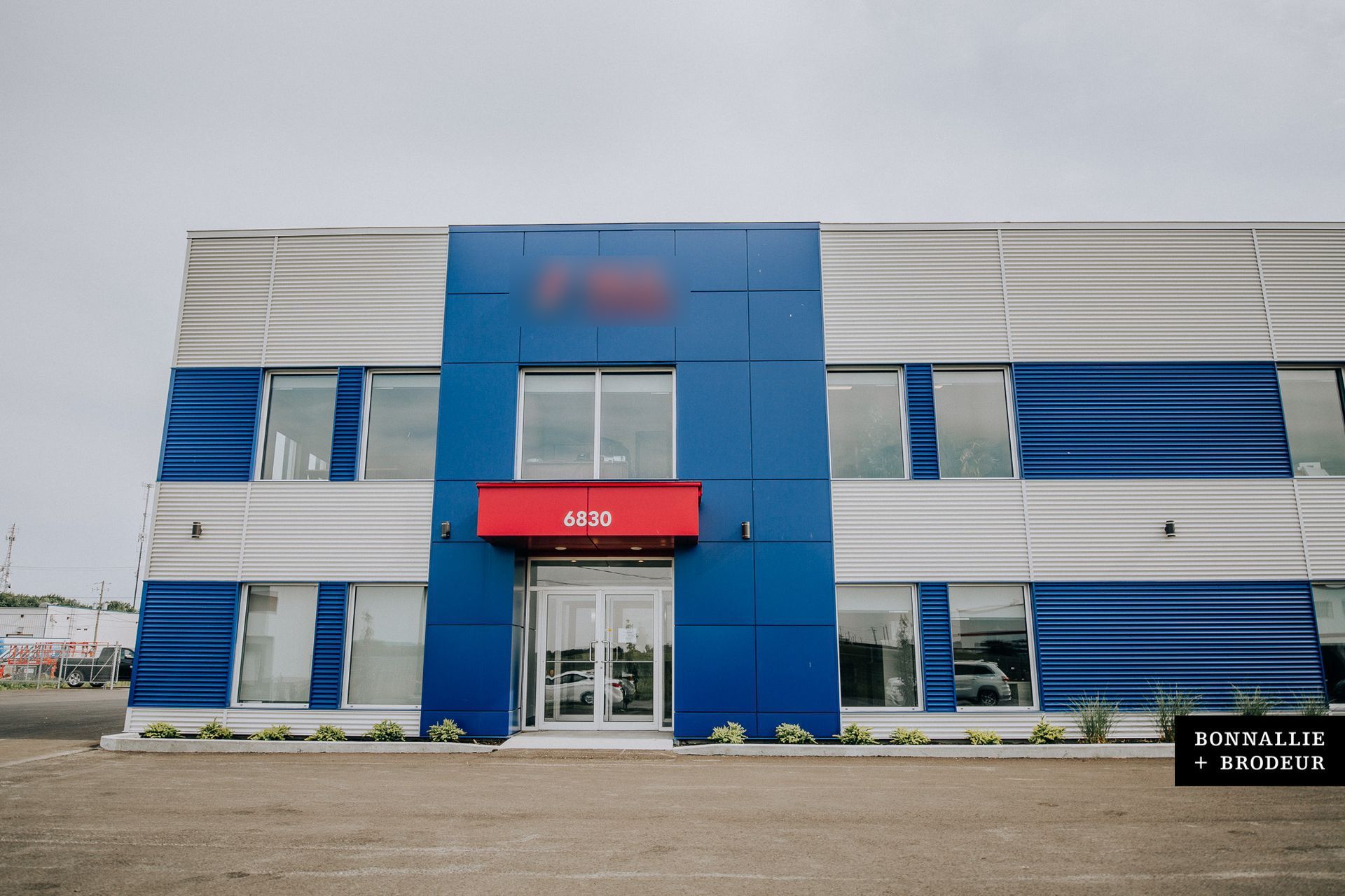 Modern blue-and-white office building with a red entrance sign and glass doors