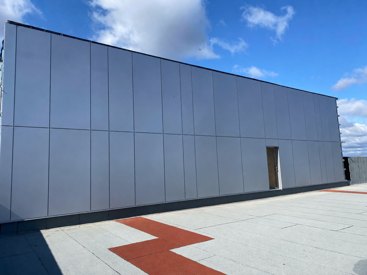 Modern rooftop with silver wall panels, scaffolding, and a red zigzag walkway under a blue sky