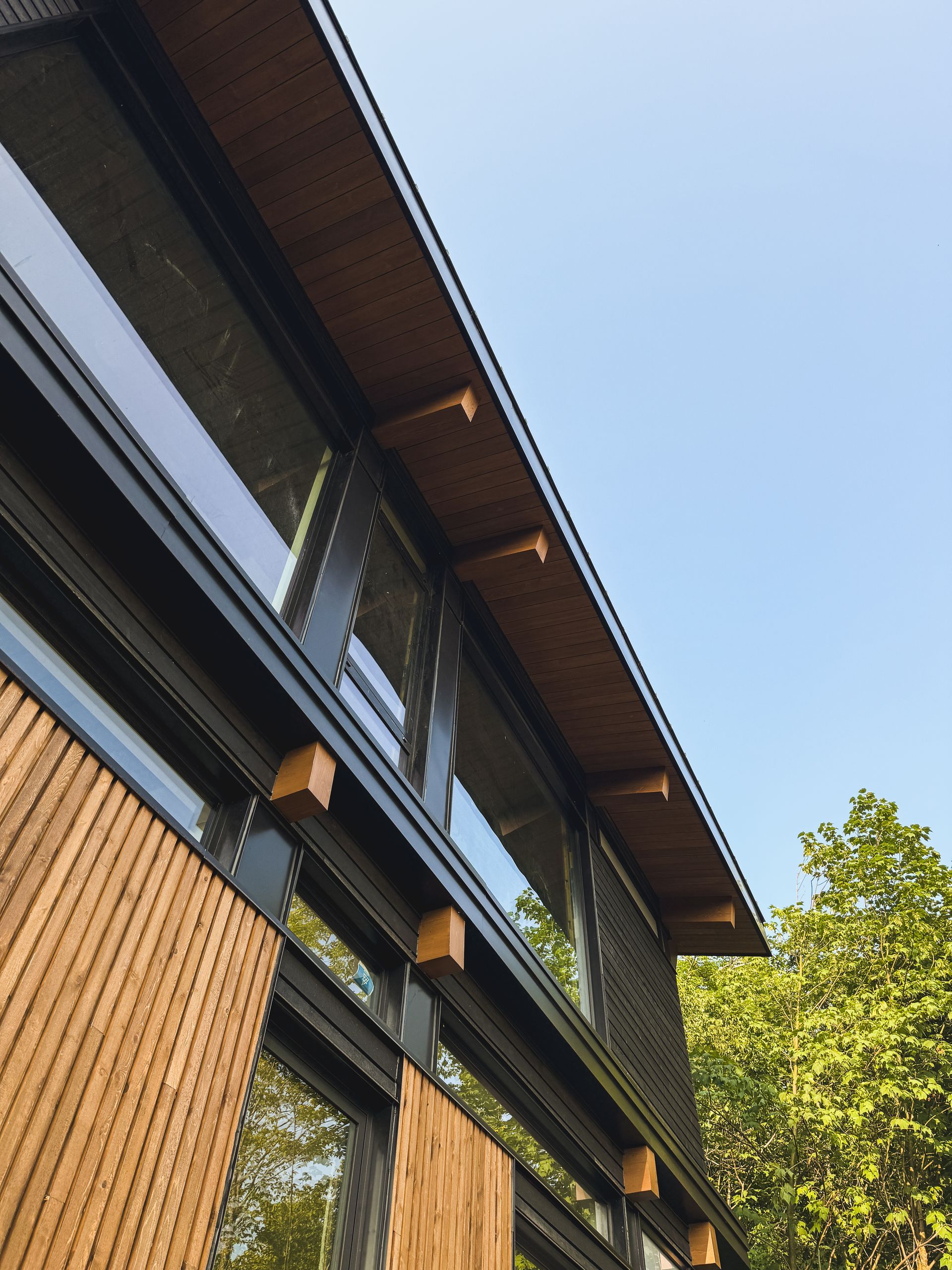 Modern building facade with wood slats, dark trim, and large windows against a blue sky