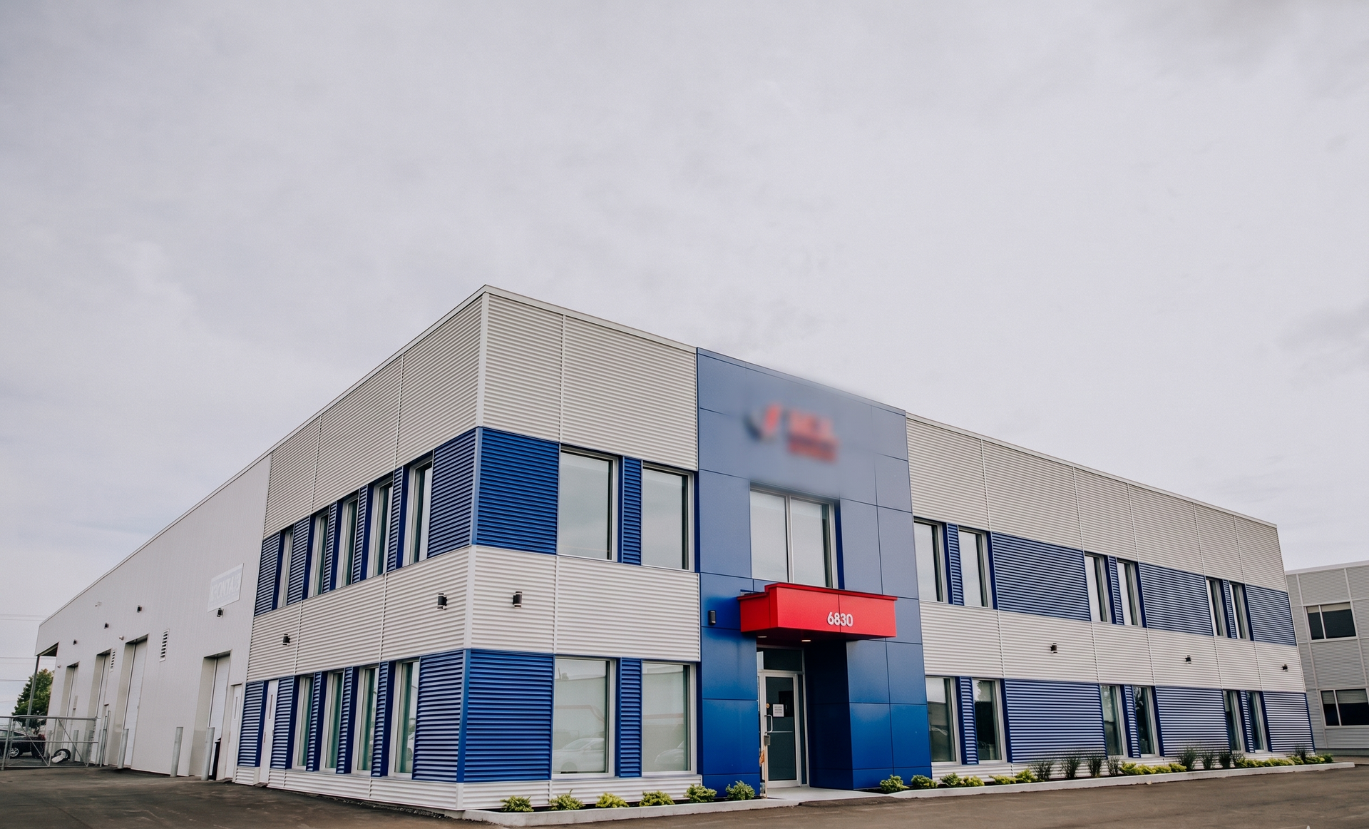Modern white-and-blue commercial building with a red entrance canopy under an overcast sky