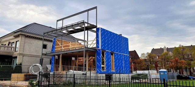 Partially built house with blue sheathing and exposed framing behind a black fence