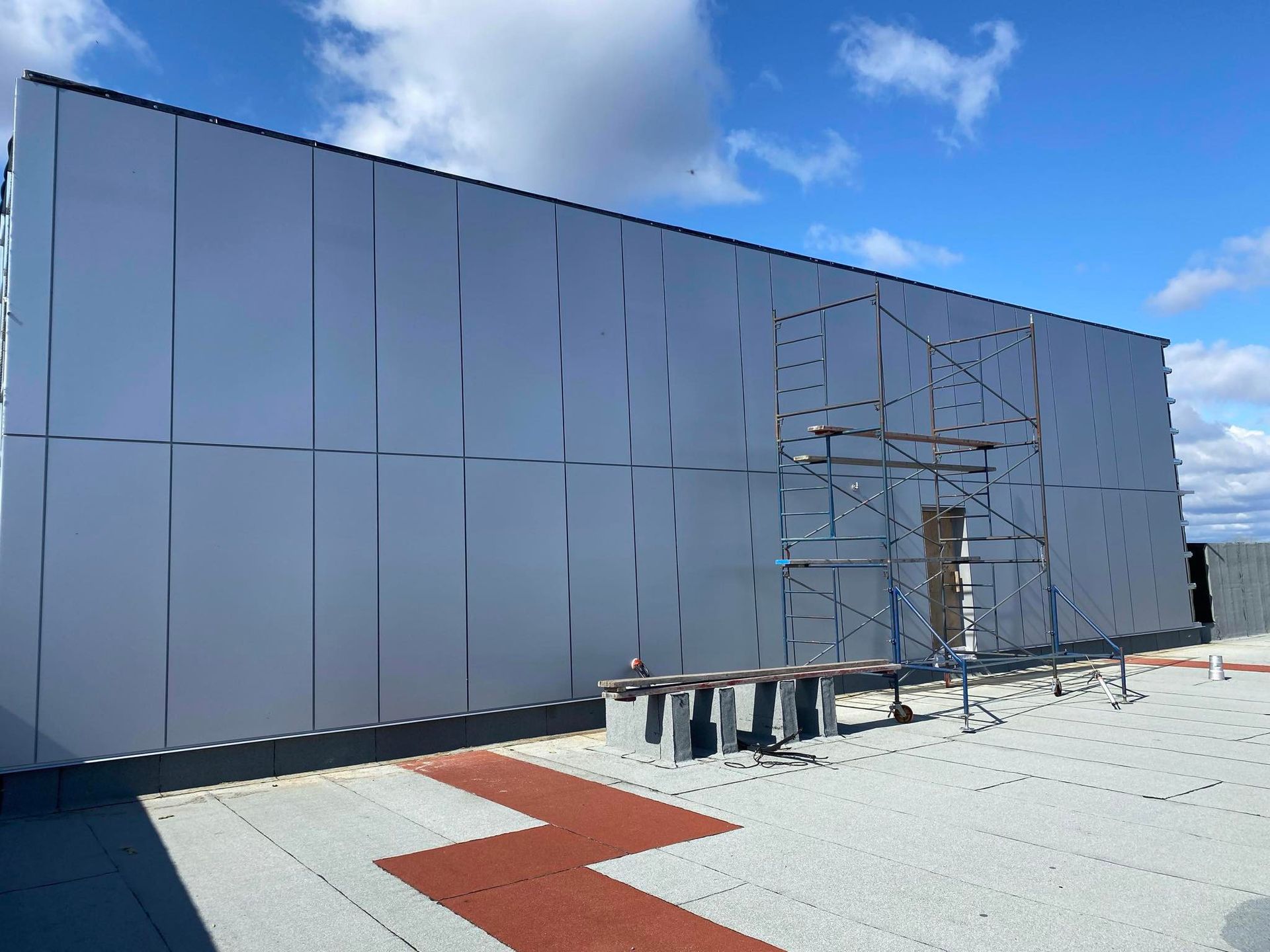 Modern rooftop with silver wall panels, scaffolding, and a red zigzag walkway under a blue sky