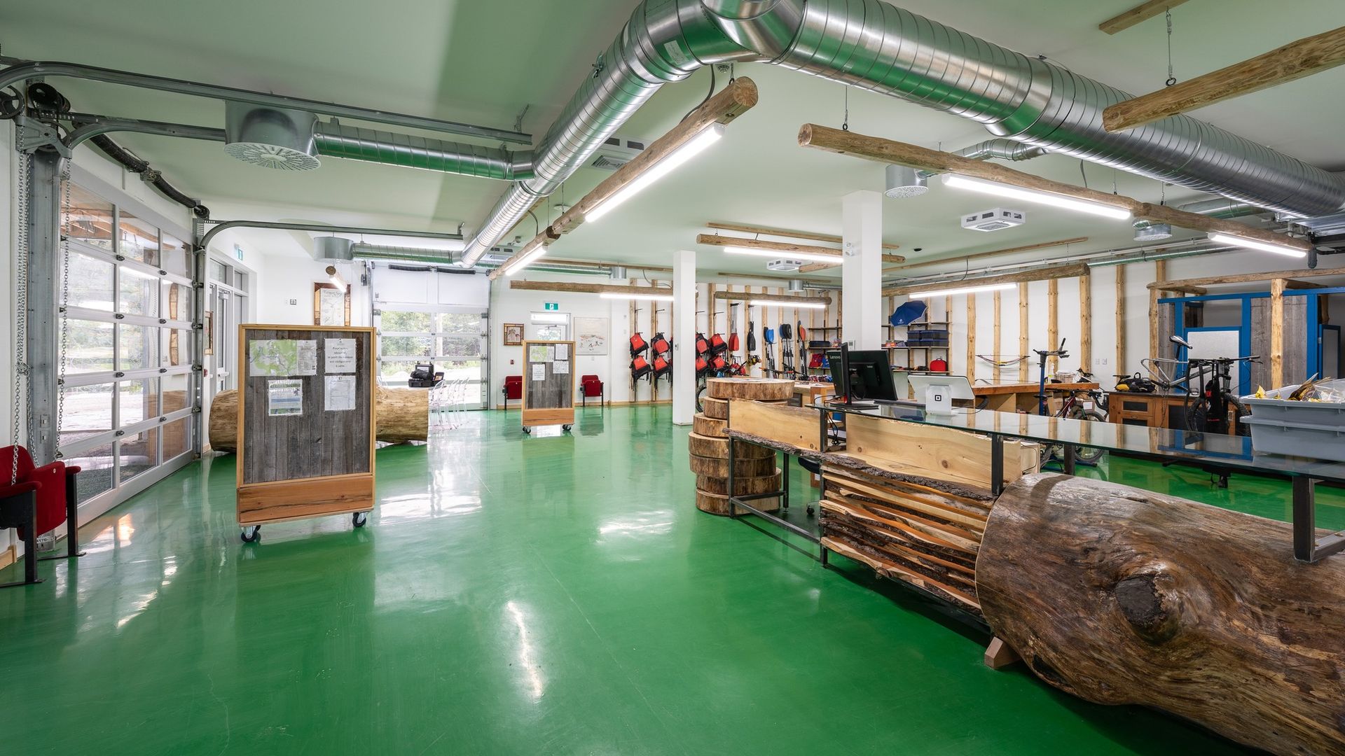 Spacious factory floor with green epoxy floor, machinery, workbenches, and stacked materials under fluorescent lights
