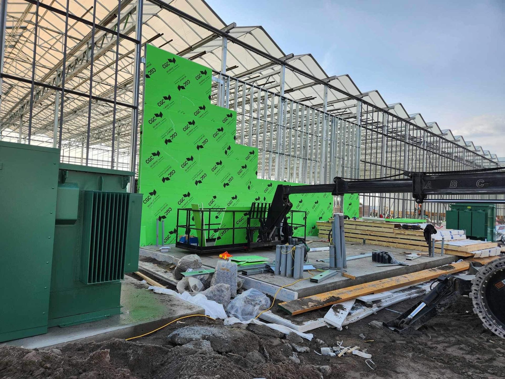 Serre partiellement construite avec panneaux d'isolation verts, échafaudages et matériaux de construction à l'intérieur