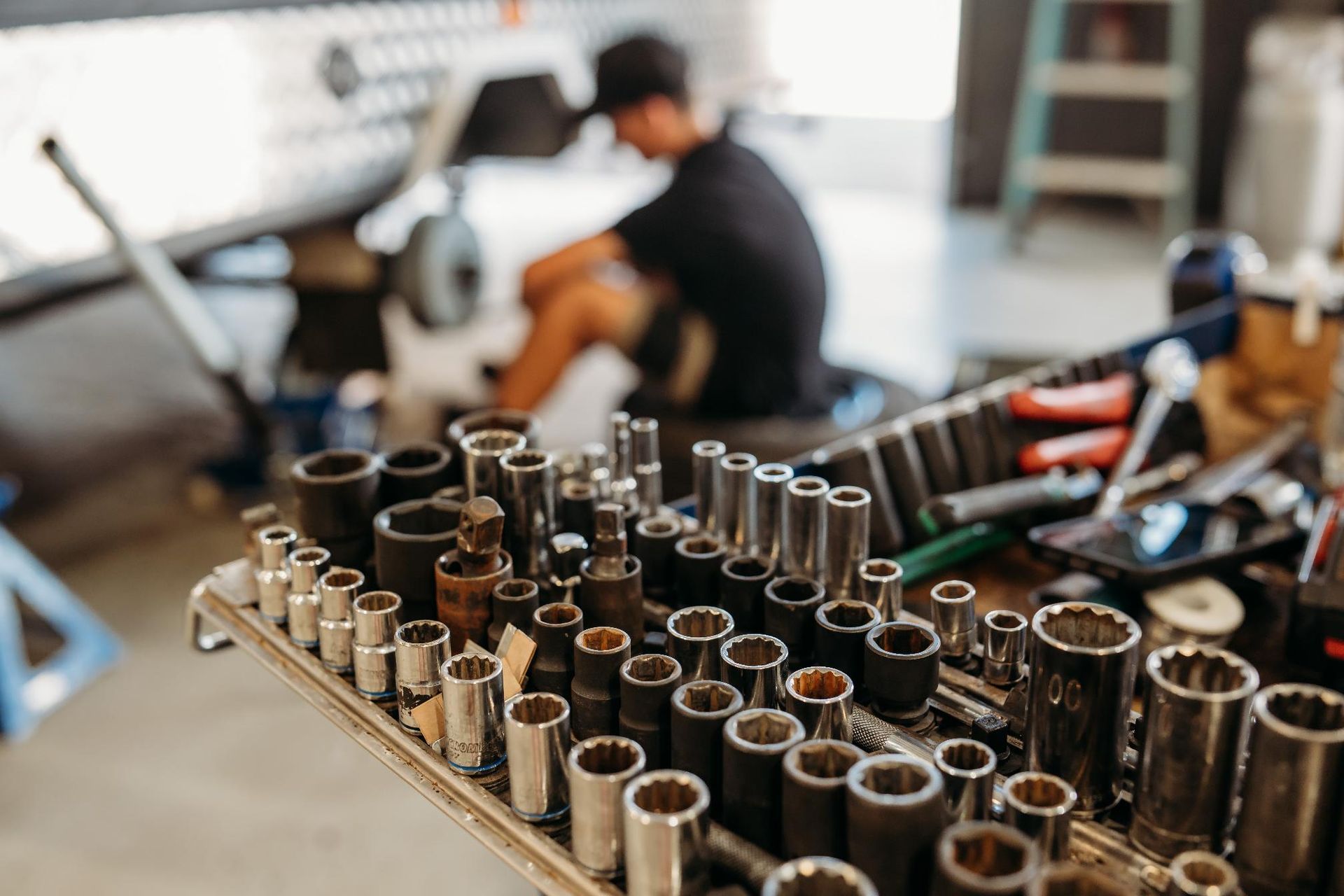 A man is sitting on the floor in a garage working on a car — Signature Mechanical In South Gladstone, QLD