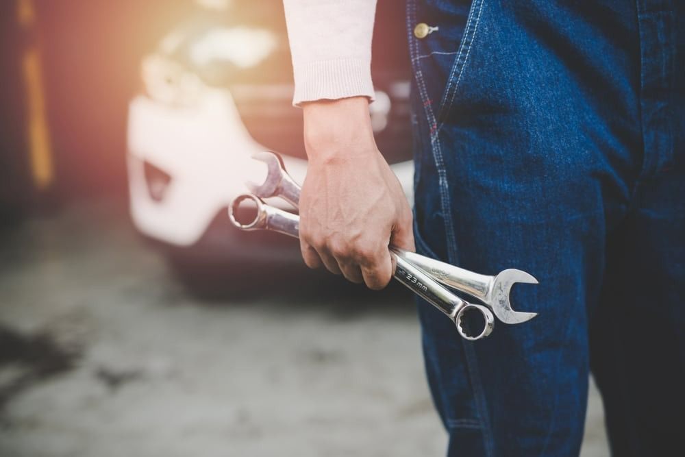 A Man Is Holding Two Wrenches In His Hands In Front Of A Car — Signature Mechanical In South Gladstone, QLD