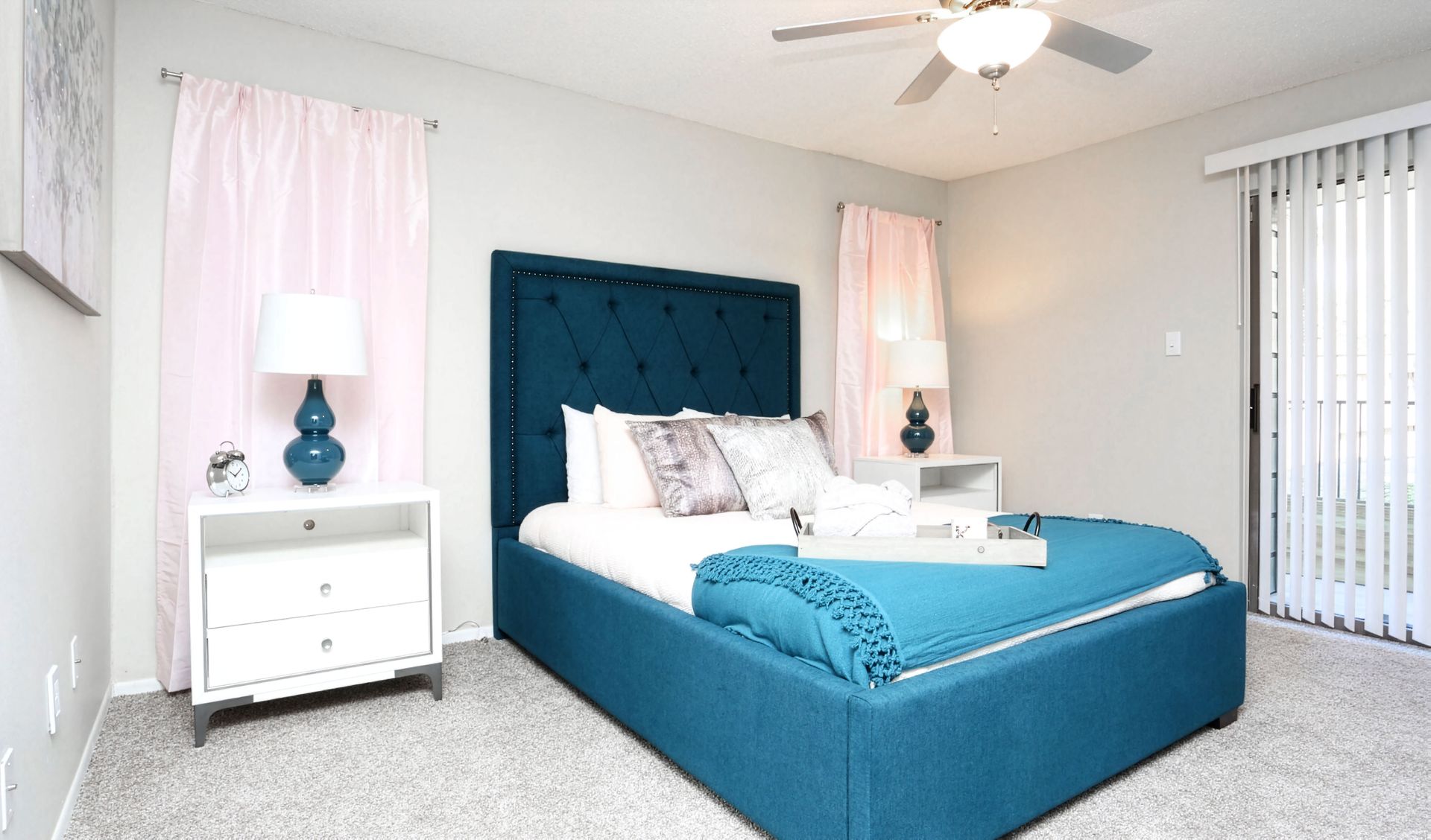 Bright bedroom with teal bed, white furniture, pink curtains, and carpeted floor