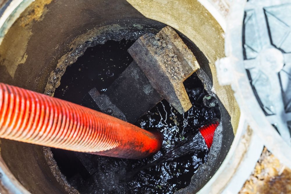 Looking down into a sewage manhole with a red hose and dark sludge.