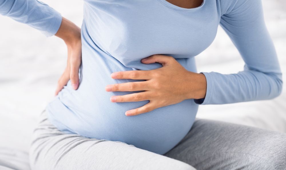 Person holding their lower abdomen and back while sitting on a bed, suggesting pain or discomfort