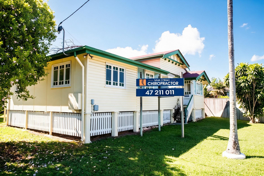 Blue chiropractic clinic sign on a cream house with green trim and phone number 47 211 011