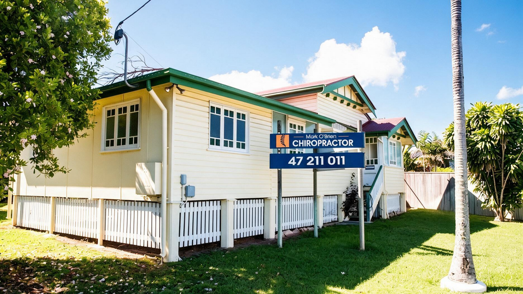 Small cream house with white fence and real estate sign on a sunny lawn.