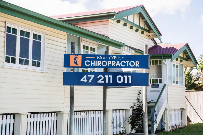 Blue chiropractic clinic sign on a cream house with green trim and phone number 47 211 011
