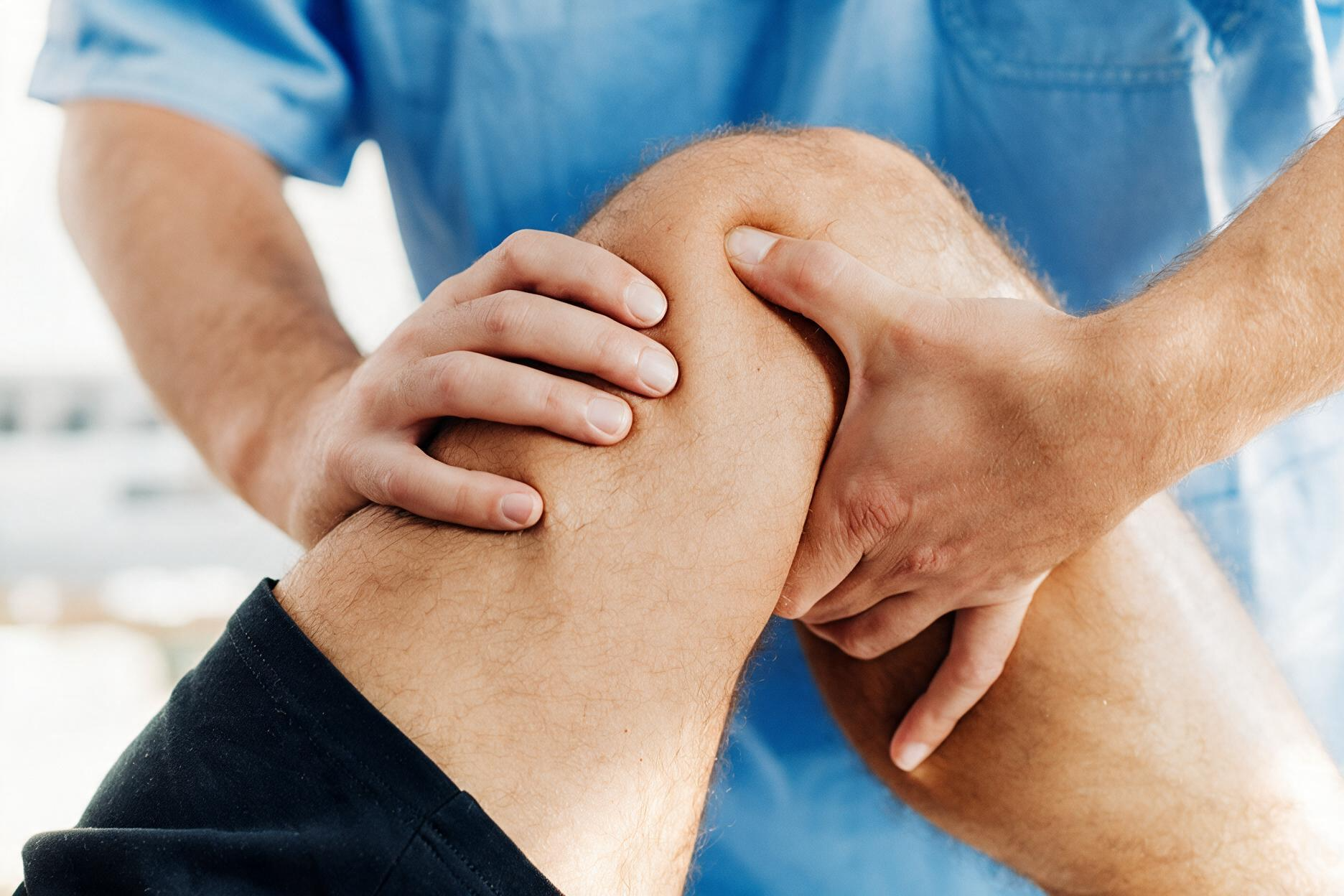 Physical therapist examining a patient’s bent knee during treatment, close-up view