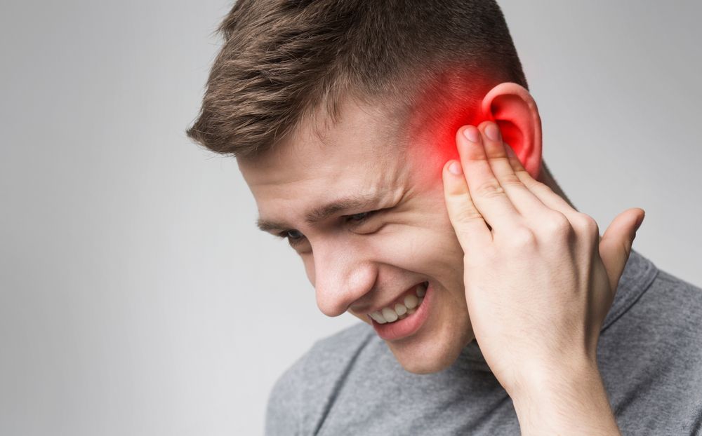 Man holding his ear and grimacing, with a red glow indicating ear pain