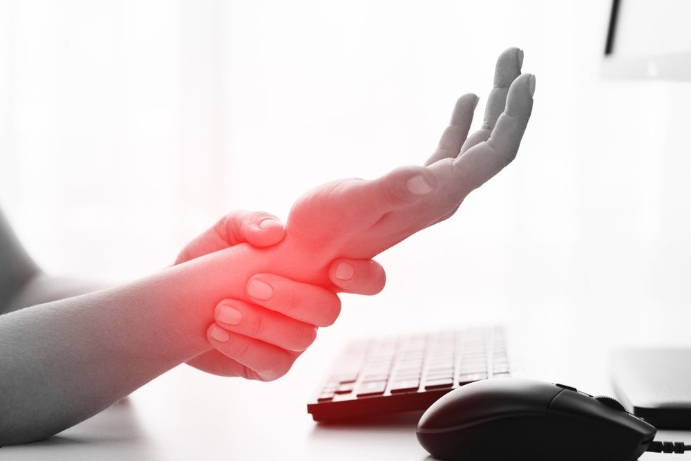 Hand holding wrist with red pain glow near keyboard and mouse on a desk