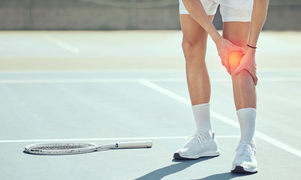Tennis player holding knee in pain on court, with racket lying nearby.