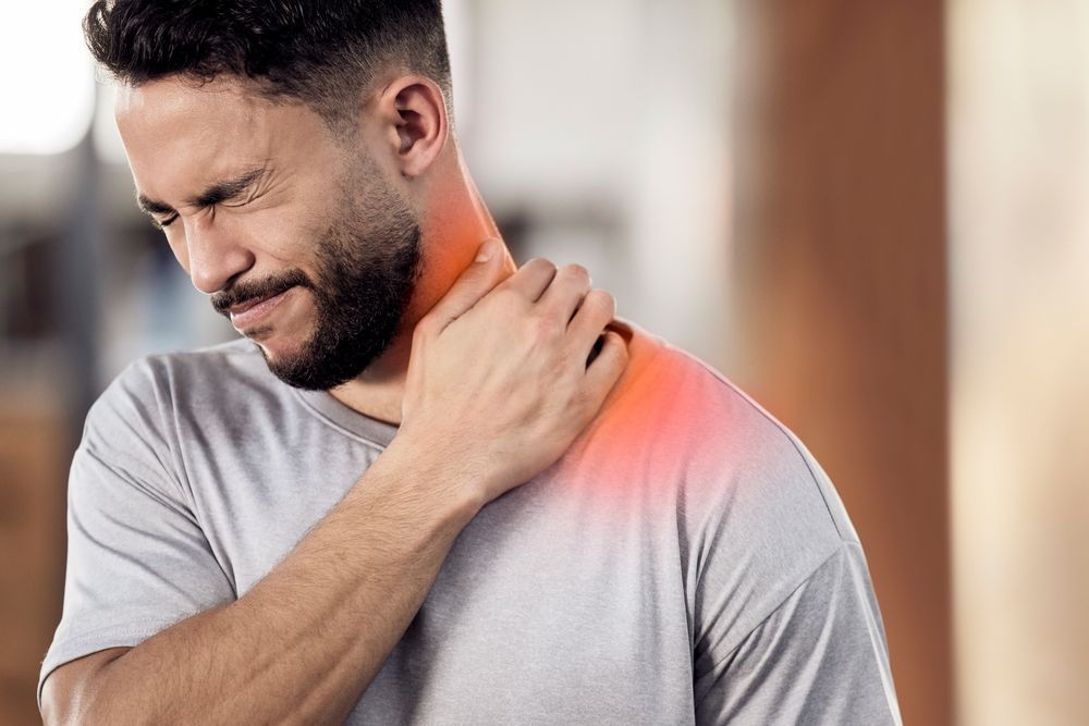 Man grimacing and holding his shoulder, with a red glow indicating pain