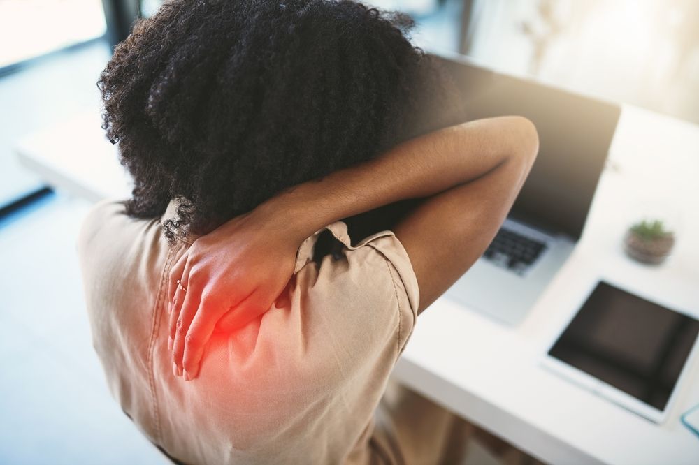 Person rubbing neck with red pain highlight while sitting at a desk with computer screen