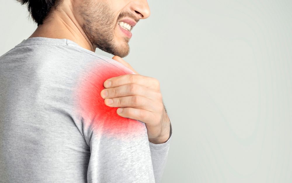 Man clutching shoulder with red pain highlight, suggesting shoulder injury or discomfort