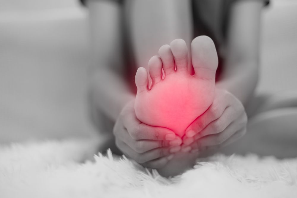 Hands holding a foot with a glowing red pain area on the sole, resting on a fluffy white surface