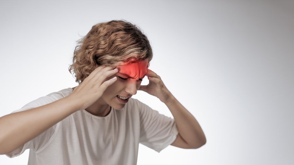 Person holding a red cloth to their forehead with a pained expression against a gray background
