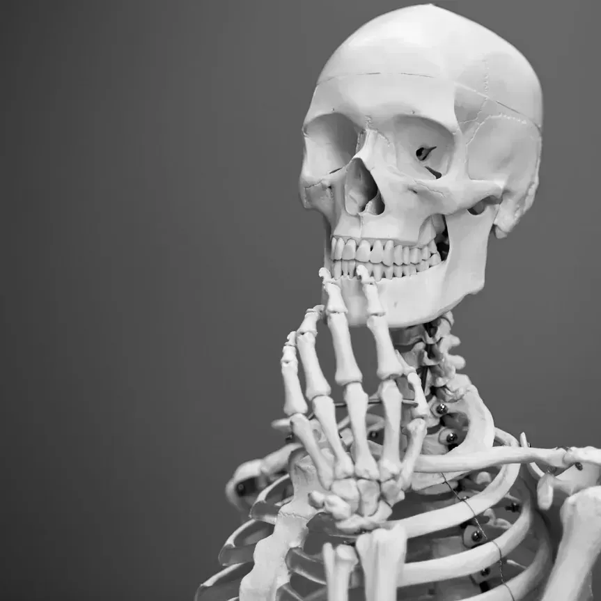 Skeleton with hand on chin, posing thoughtfully against a gray background