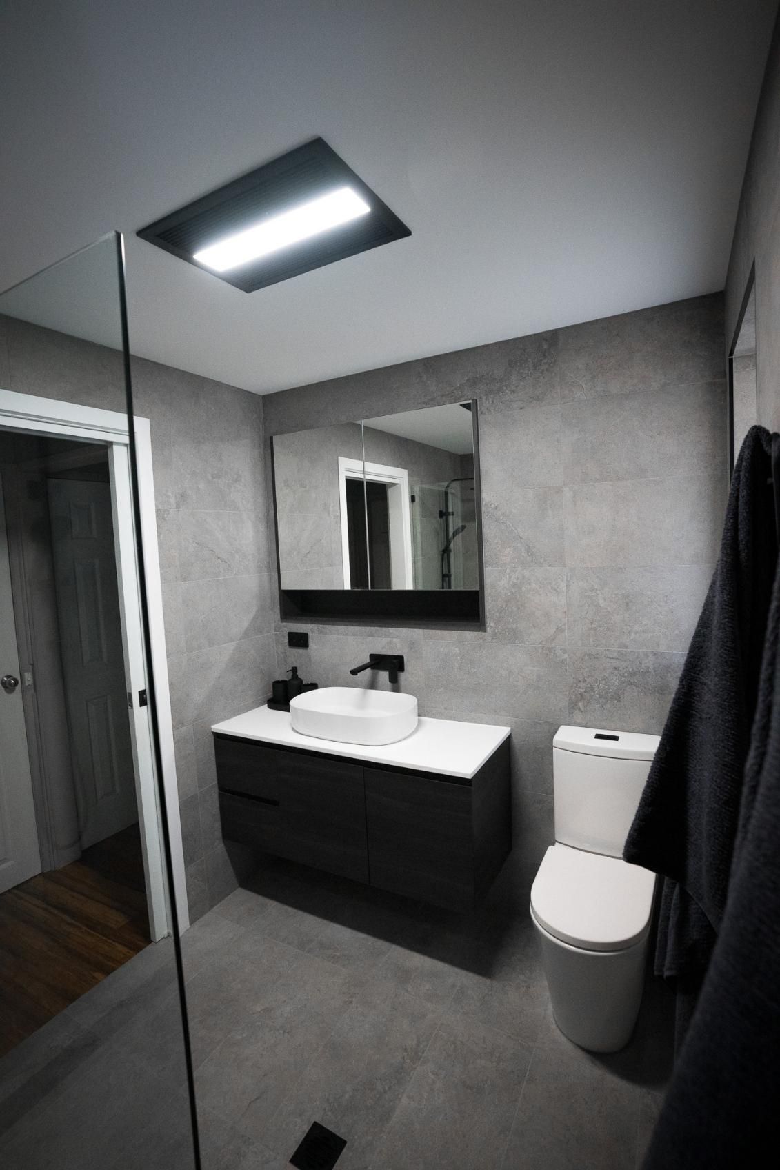 Modern Grey Bathroom With Floating Vanity, Toilet, Mirror, and a Skylight — J&C Quality Construction in Goulburn, NSW