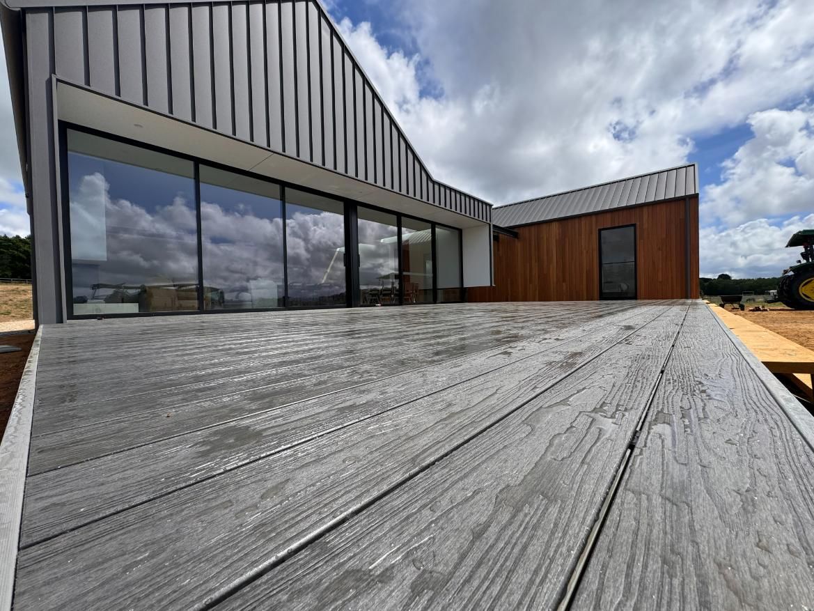 A Grey-painted House With a Large Wooden Deck on a Sunny Day — J&C Quality Construction in Goulburn, NSW