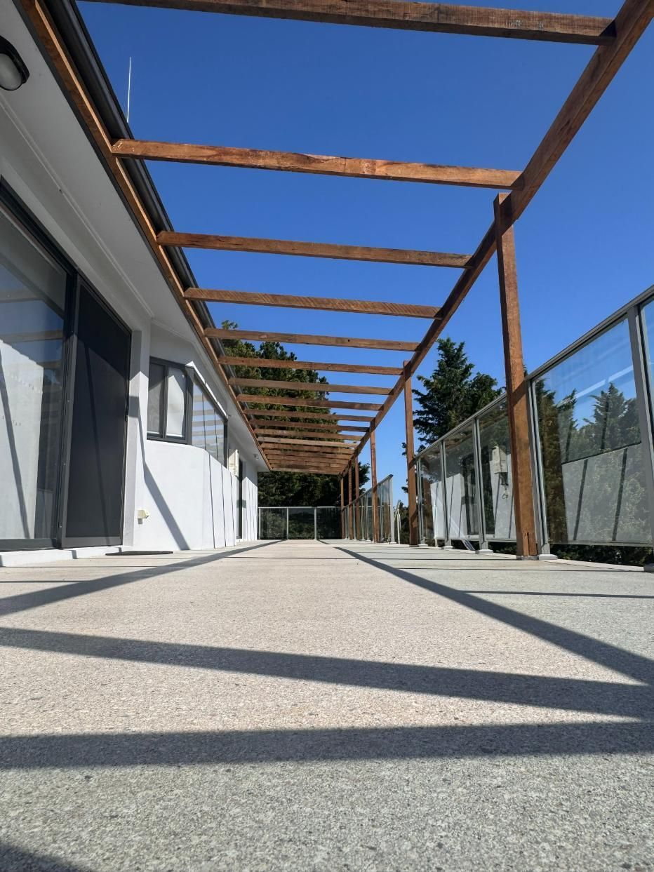 A Long Concrete Patio With a Wooden Pergola Overhead — J&C Quality Construction in Goulburn, NSW