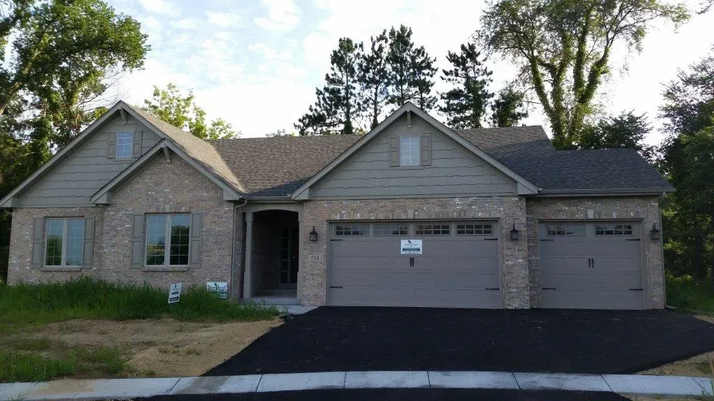 A one-story brick house with a gray roof and garage doors. A black driveway.