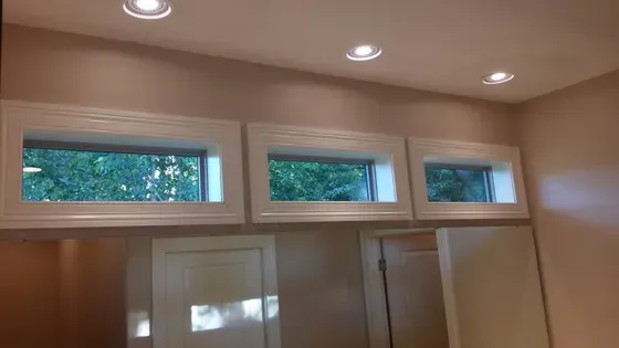 Three small rectangular windows in white trim, above closed white doors, with recessed ceiling lights
