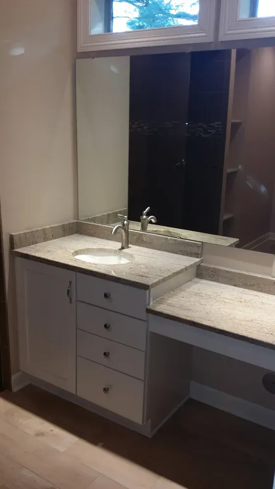Bathroom vanity with white cabinets, granite countertop, sink, and large mirror.