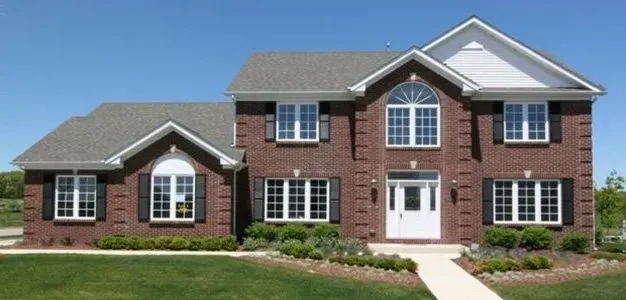 Brick two-story house with white trim, black shutters, and a green lawn on a sunny day.