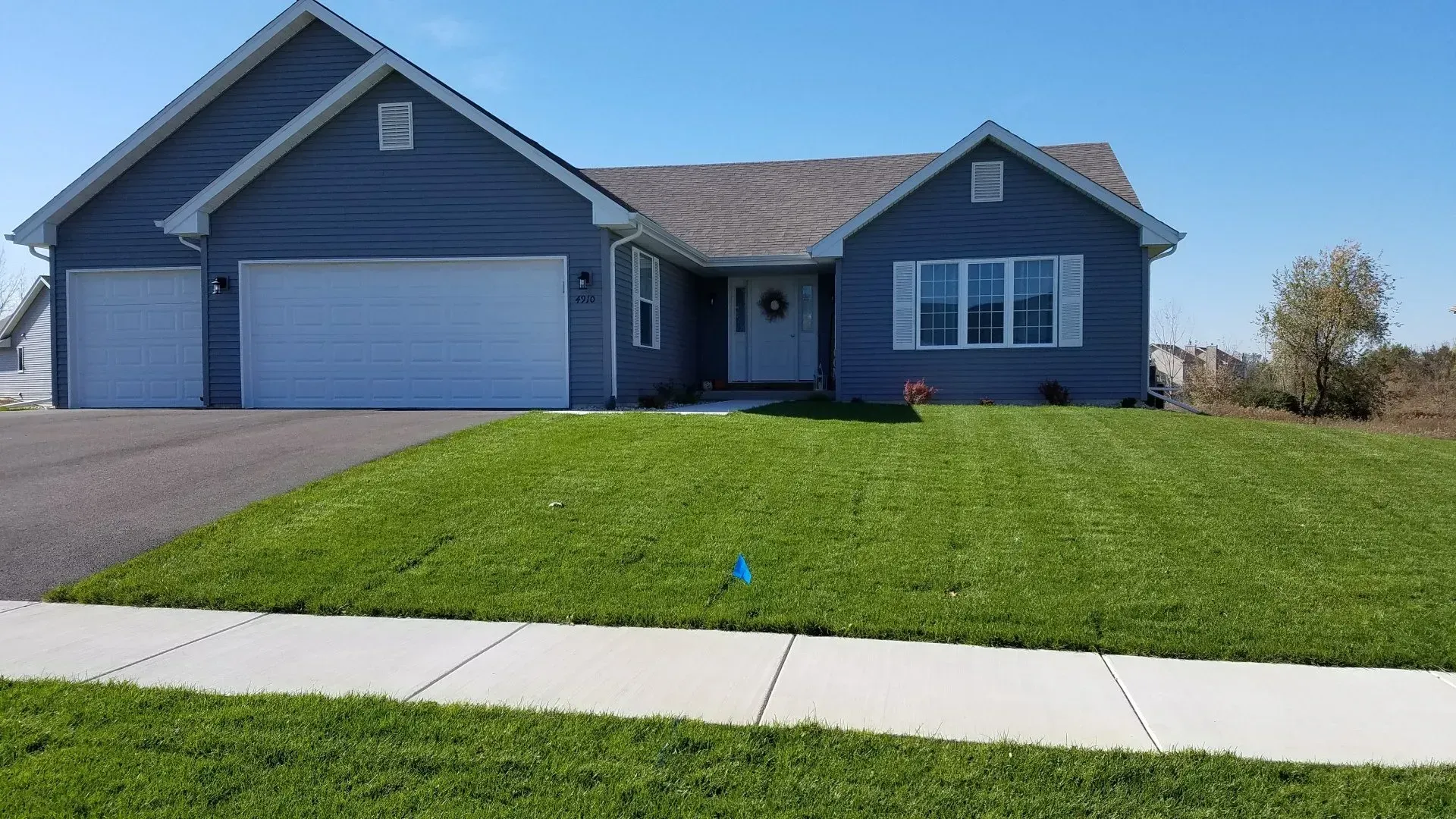 Blue house with a green lawn and a driveway on a sunny day.