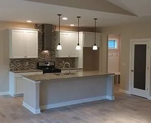 A modern kitchen with white cabinets, a gray island, pendant lights. decorative backsplash and stainless steel range hood