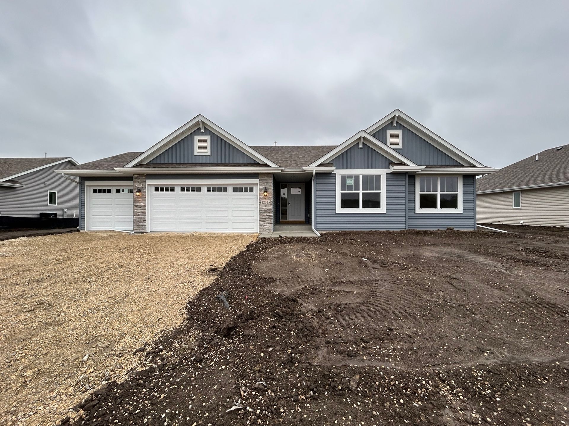 New light blue house with white trim, unfinished yard. Gray sky.